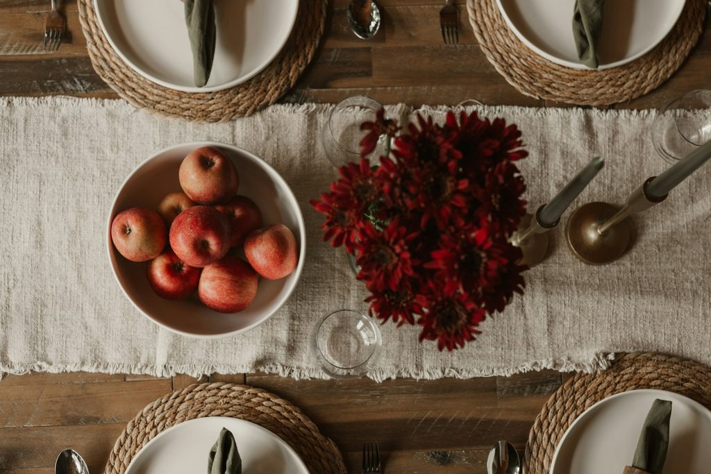 a bowl of apples on a linen table runner on a wooden table with place settings to create a fruit centerpiece that's rustic for Thanksgiving