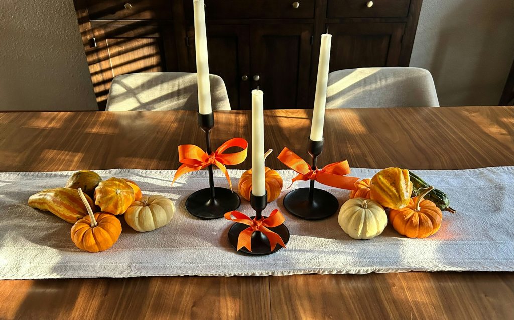 mini pumpkins on a table runner on a wooden dining room table with candlesticks wrapped with orange ribbon
